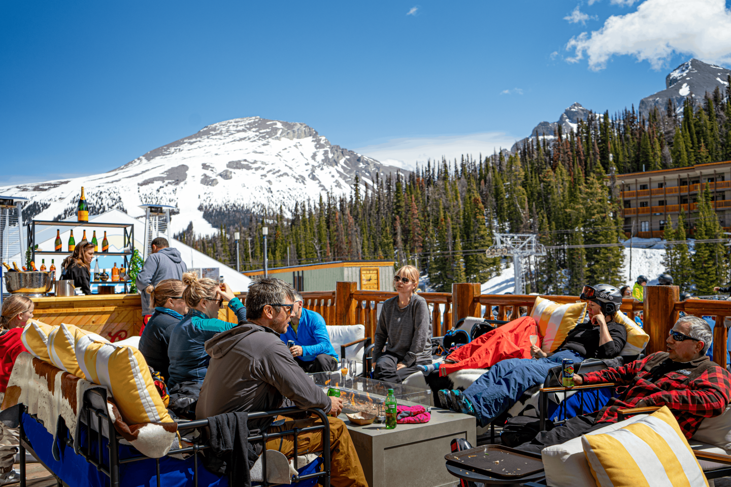 People browsing outdoor gear at a mountain market beneath snowy peaks.