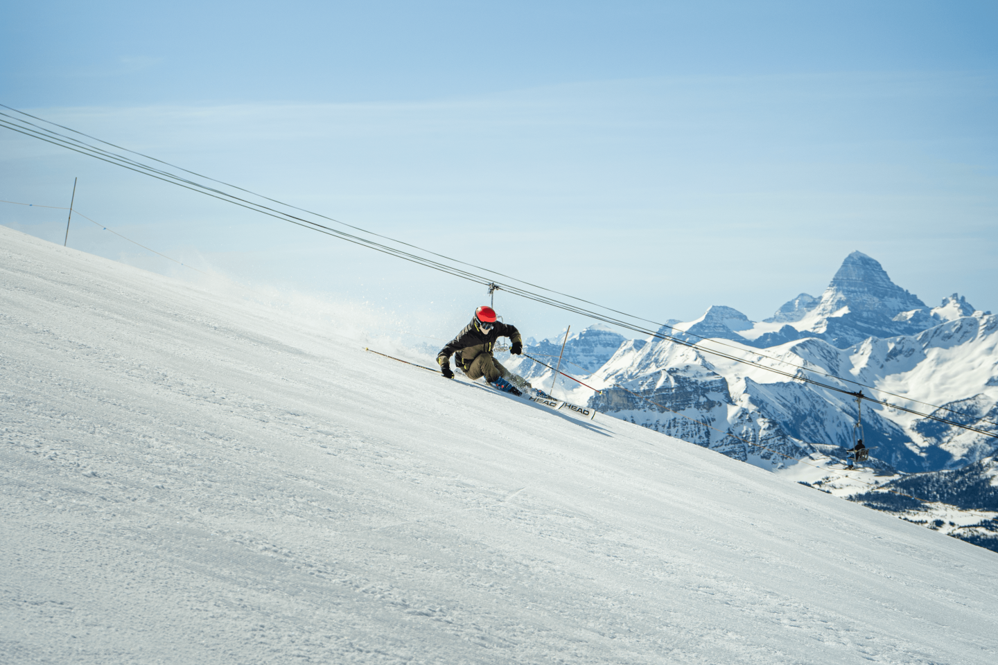 Skier carving down a snowy slope with jagged mountains in the background.