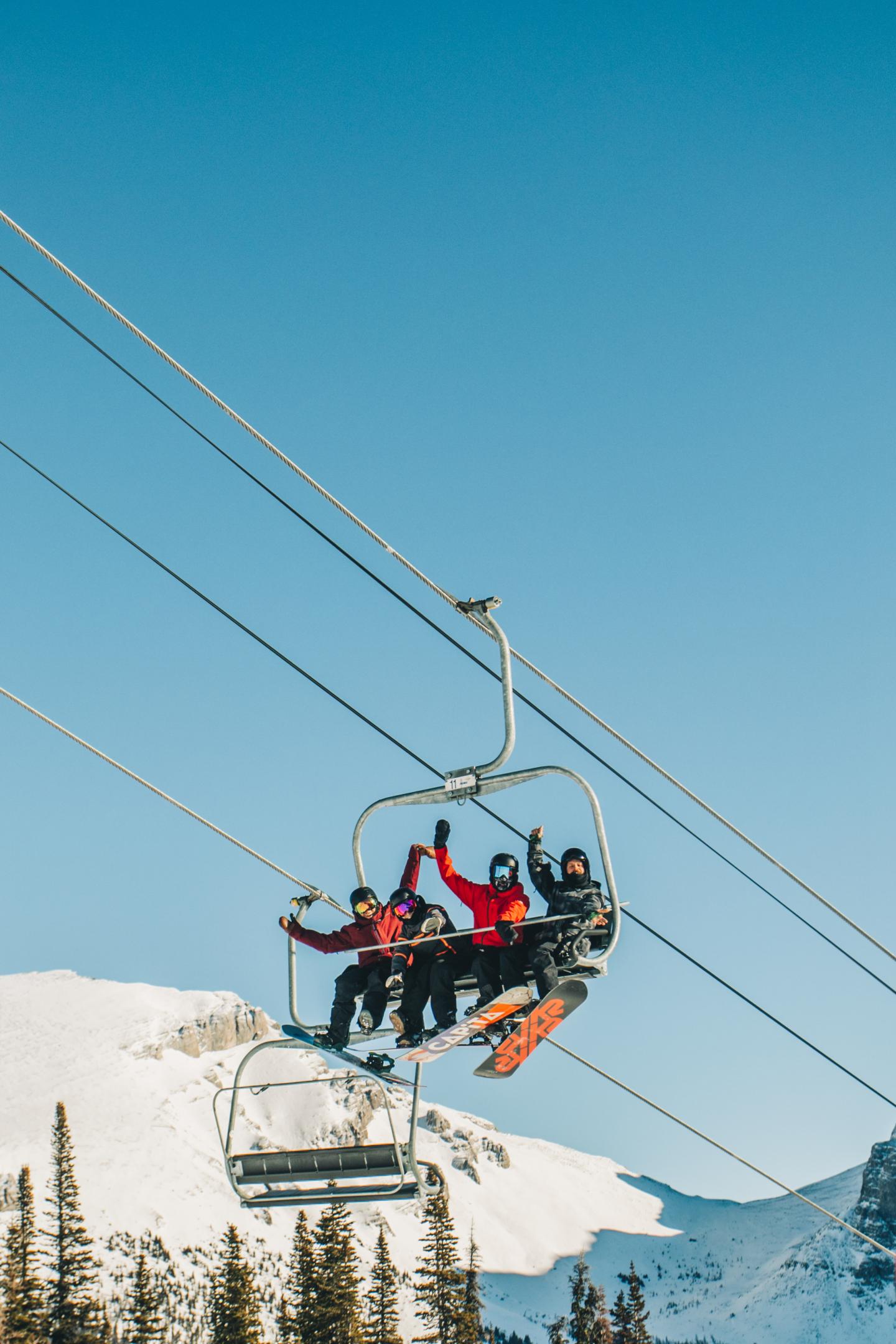 Skiers riding a chairlift over snowy mountain slopes under a clear blue sky