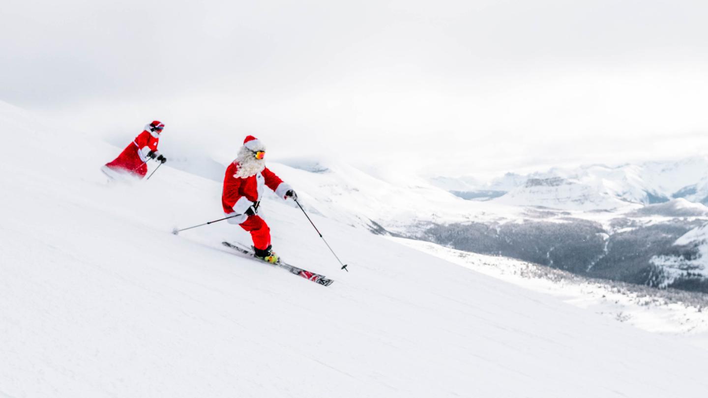 Santa and Mrs Claus skiing down a snowy mountain slope.