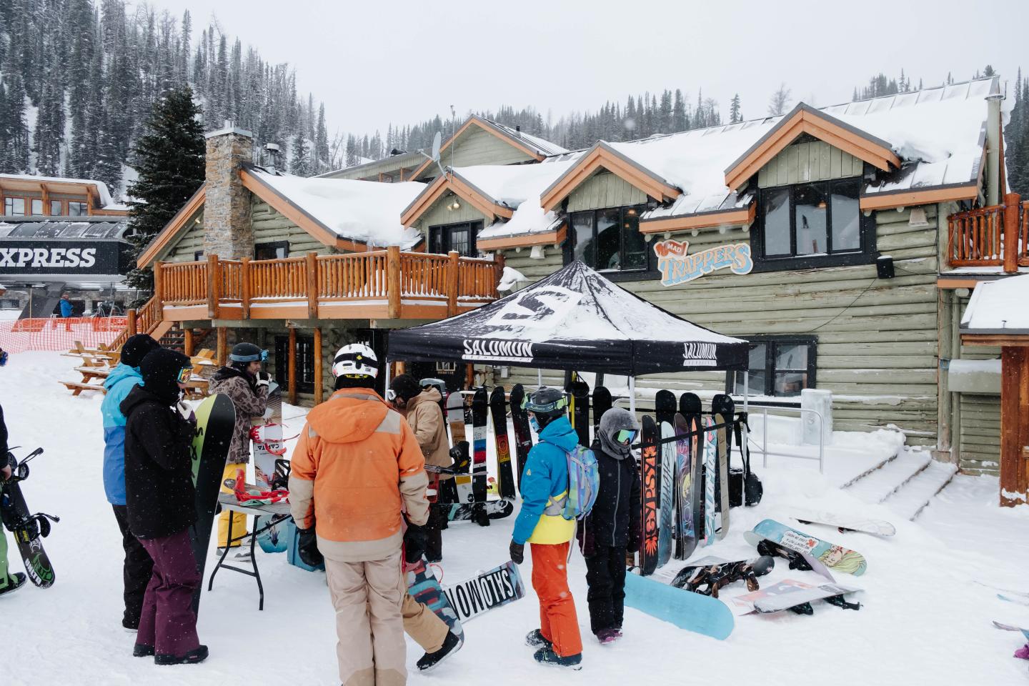 Skiers gather outside a snowy mountain lodge beside equipment racks.
