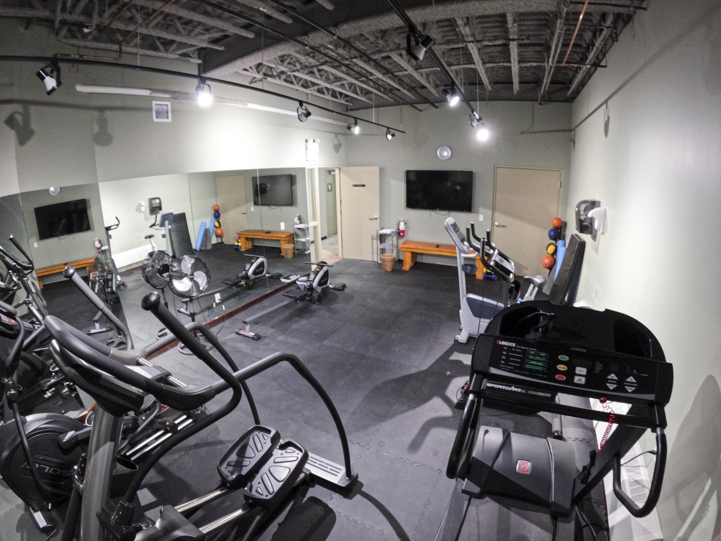 Wide-angle photo of a modern gym with treadmills, bikes, and weight benches.