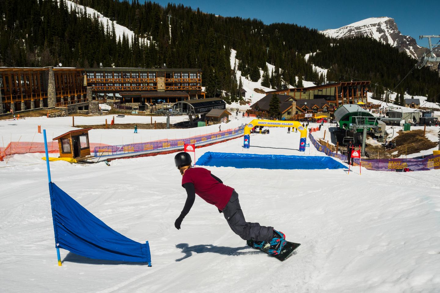 Snowboarder carving beside a blue gate on a sunny mountain slope