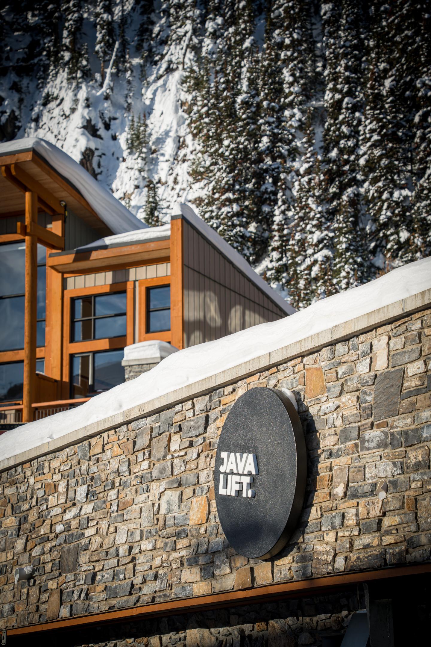 Modern wood-and-stone ski lodge beneath snow-covered evergreen trees.