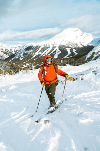Skier in orange jacket ascending snowy mountain beneath cloudy skies