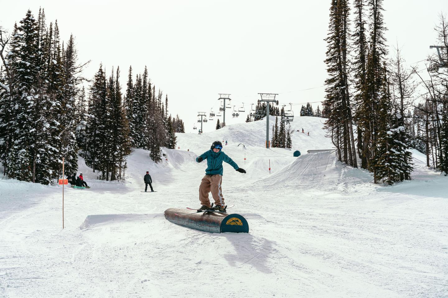 Snowboarder jumping on a snowy forest trail beneath ski lifts.