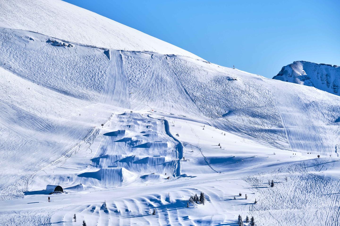 Snow-covered mountain slope with ski tracks under a clear blue sky.