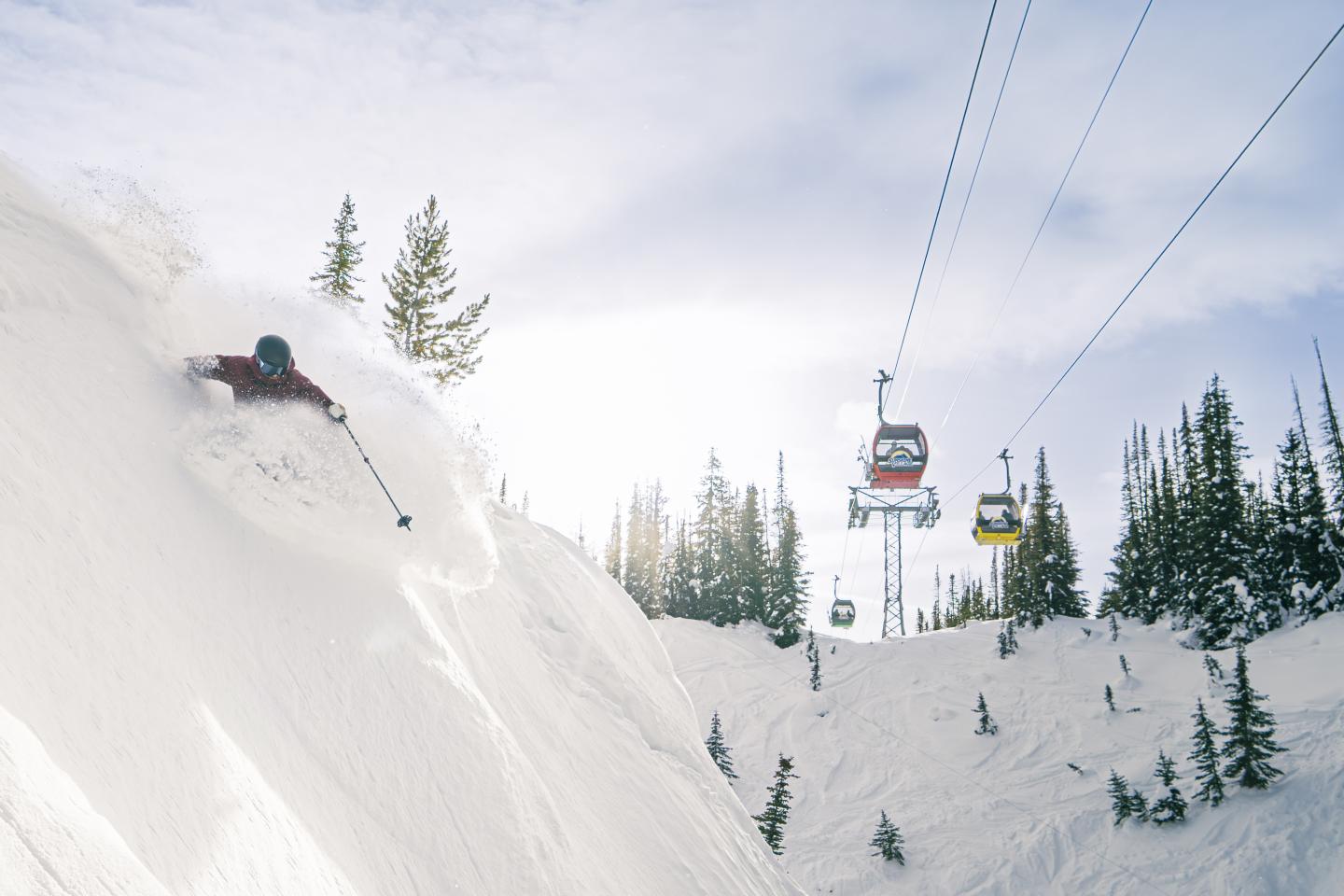 Skier carving down a snowy slope beneath a chairlift.
