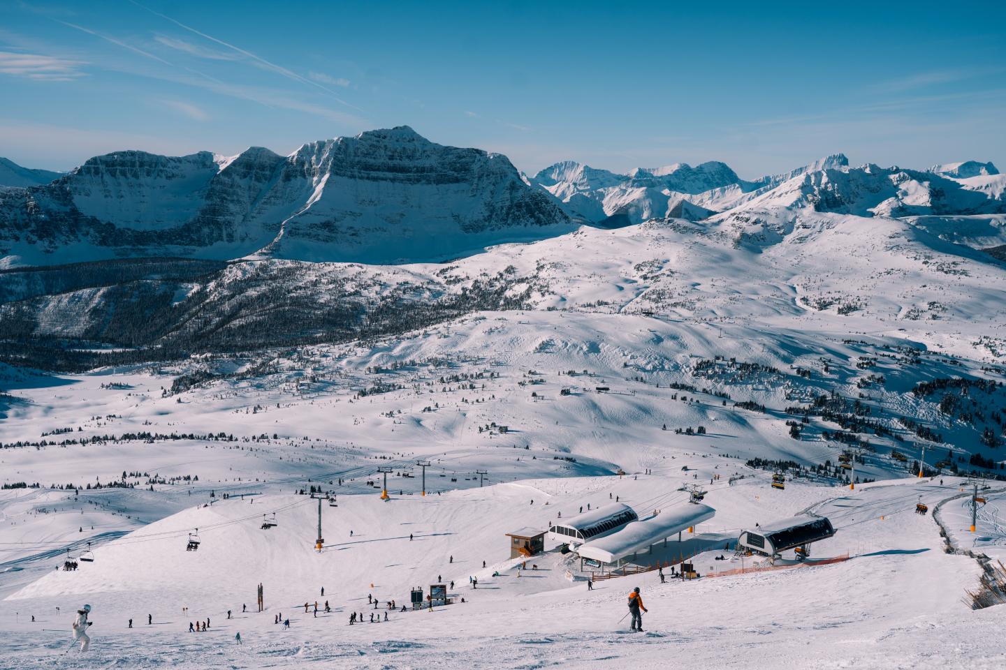 Snow-covered mountain range and ski slopes under a clear blue sky.