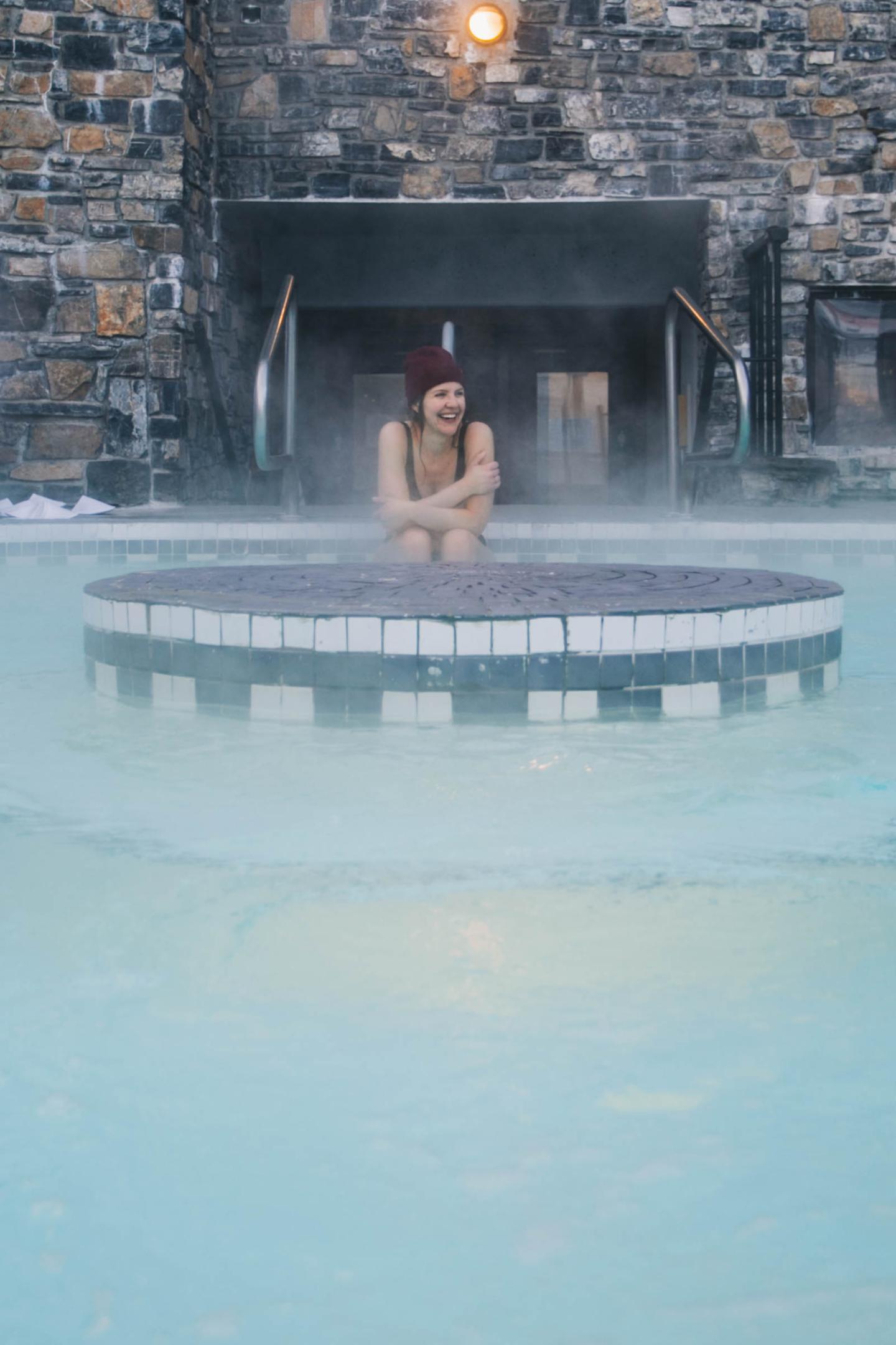 Woman sitting in a steaming pool before a stone wall.