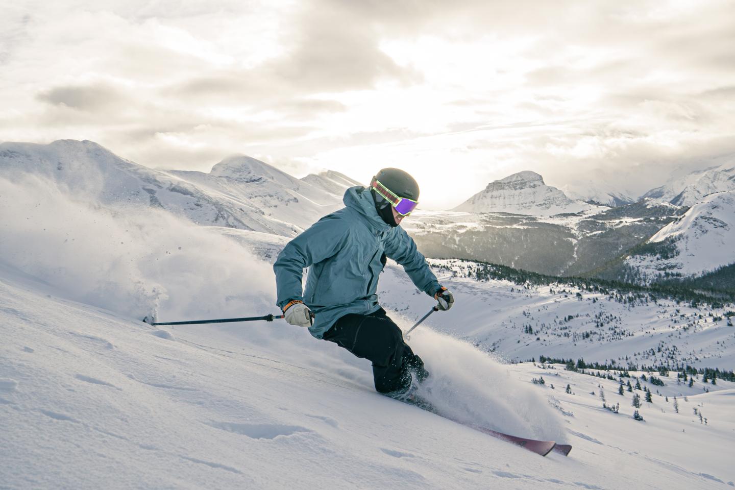 Skier carving down a snowy mountain slope beneath cloudy skies.