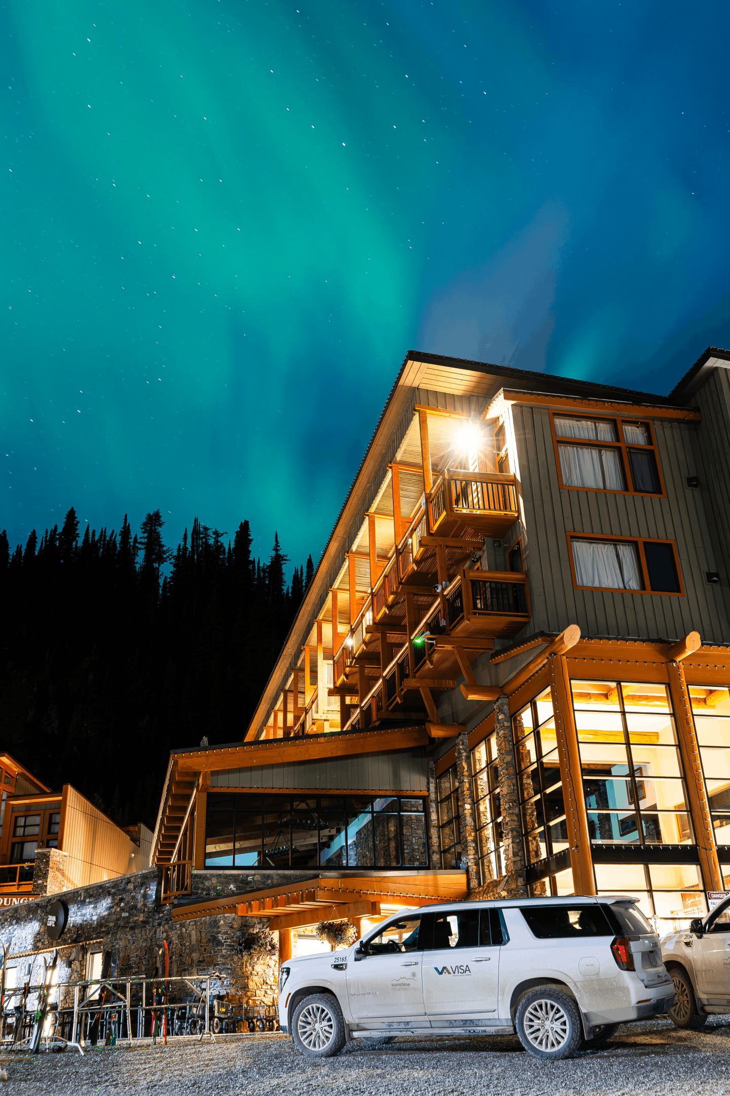 Snowy mountain lodge glowing at dusk, with white SUV parked outside