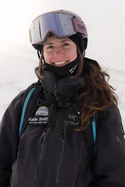 Smiling skier in goggles and black jacket on a snowy slope