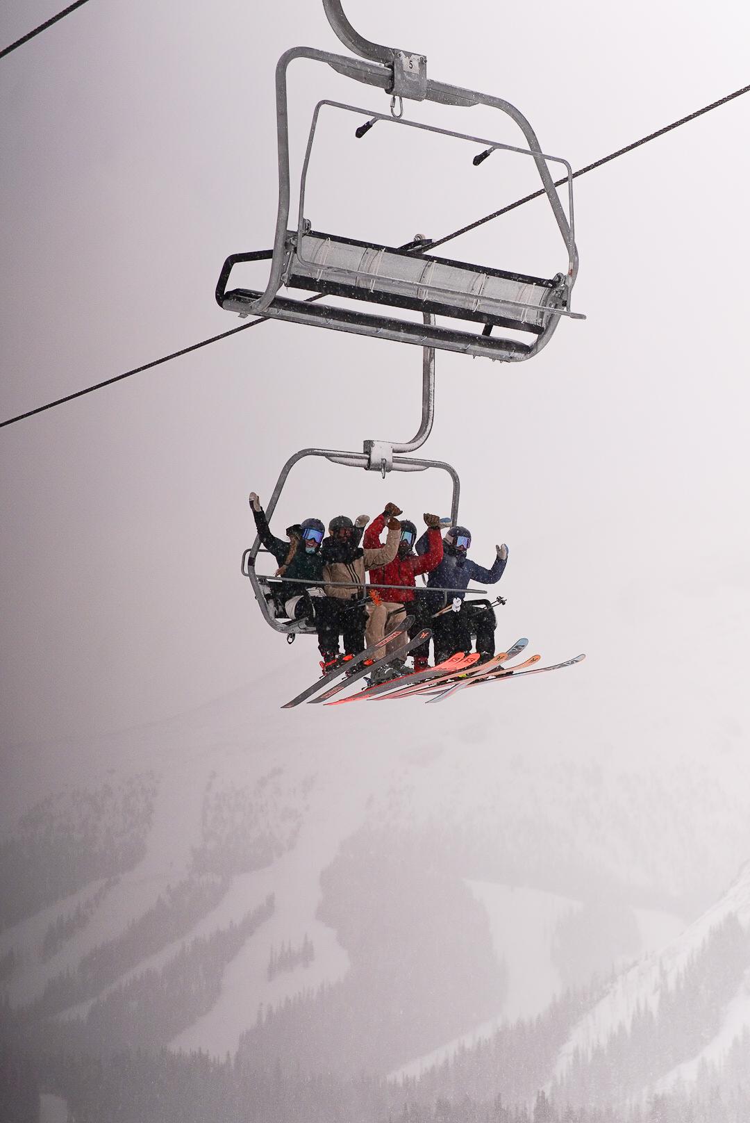 Two skiers ride a chairlift above snowy mountain slopes.