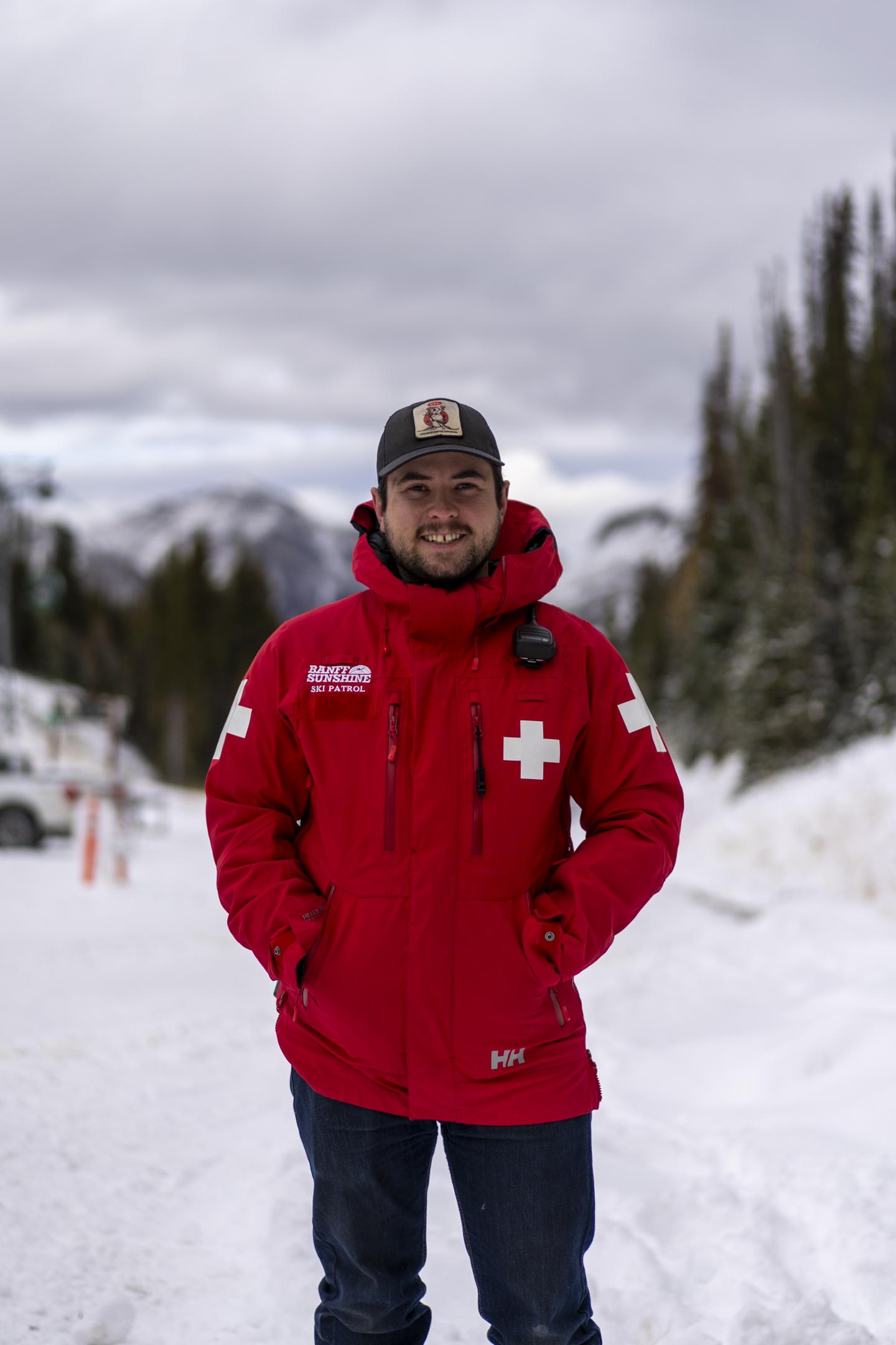 Man in red Red Ski jacket standing on a snowy trail.