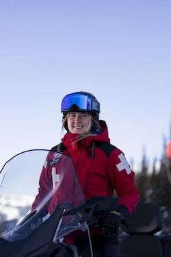 Skier in red jacket and blue helmet holding ski poles on a snowy mountain