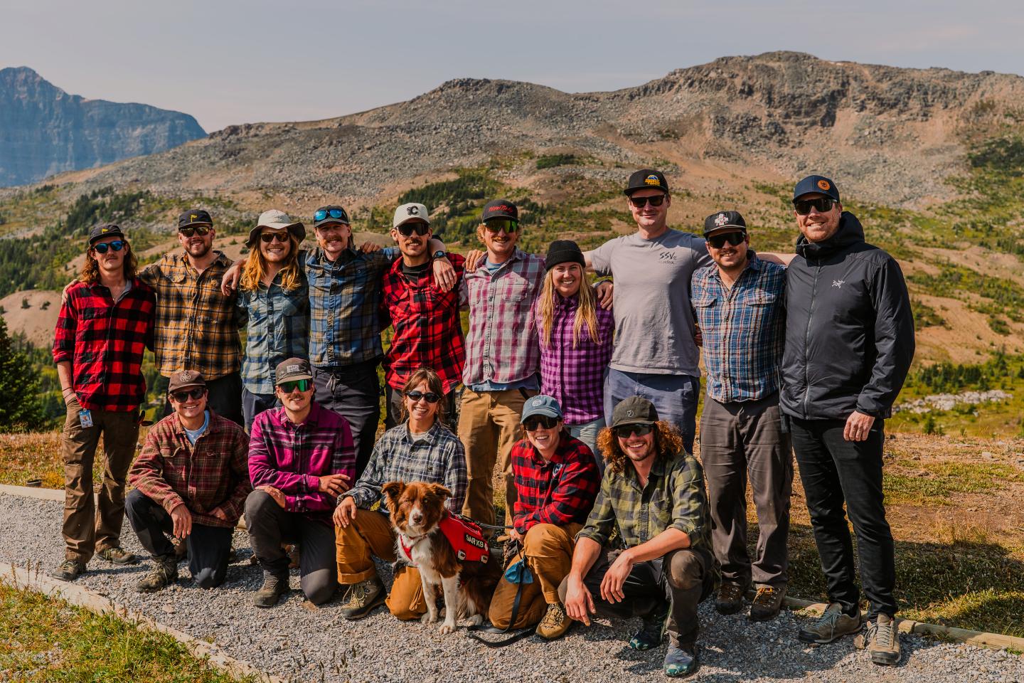 Group of hikers posing on a rocky mountain trail with rugged hills behind them.