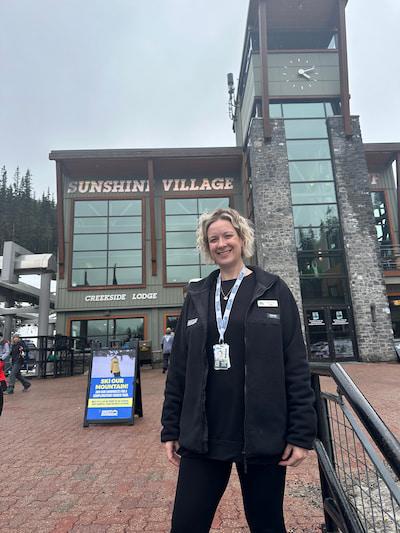 Woman standing outside Whistler Village entrance beneath snowy mountains.